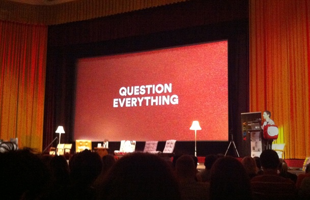 A large screen in a theatre with the message 'question everything'